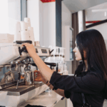 Close-up of a woman using a commercial-grade espresso machine, representing equipment financing for the hospitality and coffee industry.