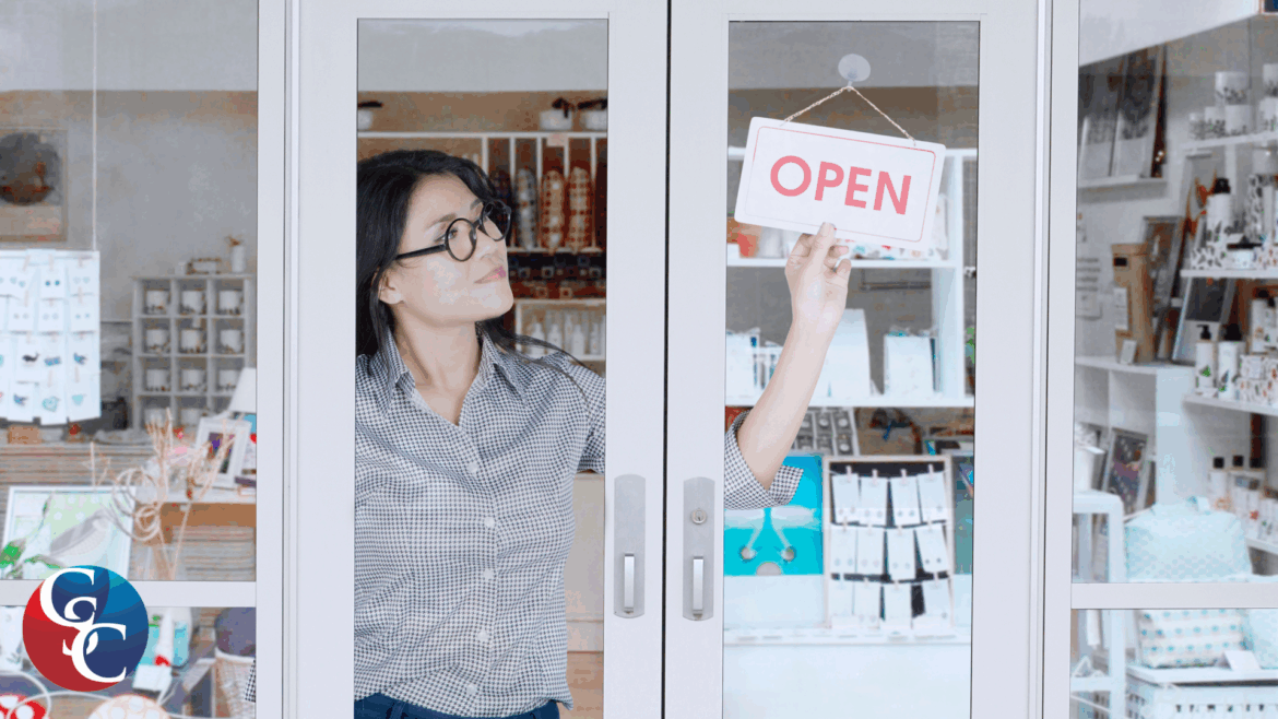 A photo of a small business owner in a storefront, adjusting an "Open" sign on a glass door.