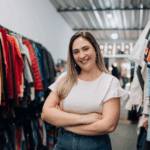 For Page 4: Thrift Store Owner Alt Text: A smiling female thrift store owner standing with crossed arms in a boutique clothing store, surrounded by racks of colorful vintage apparel.