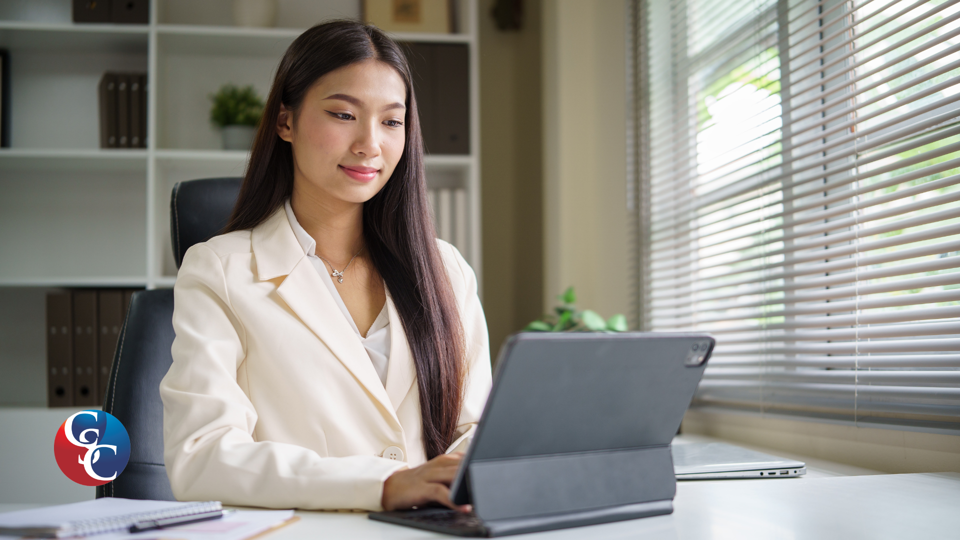A professional woman sitting at a desk with a laptop, applying for revenue-based financing. She is looking at the laptop with a friendly expression, with office shelves and documents in the blurred background.